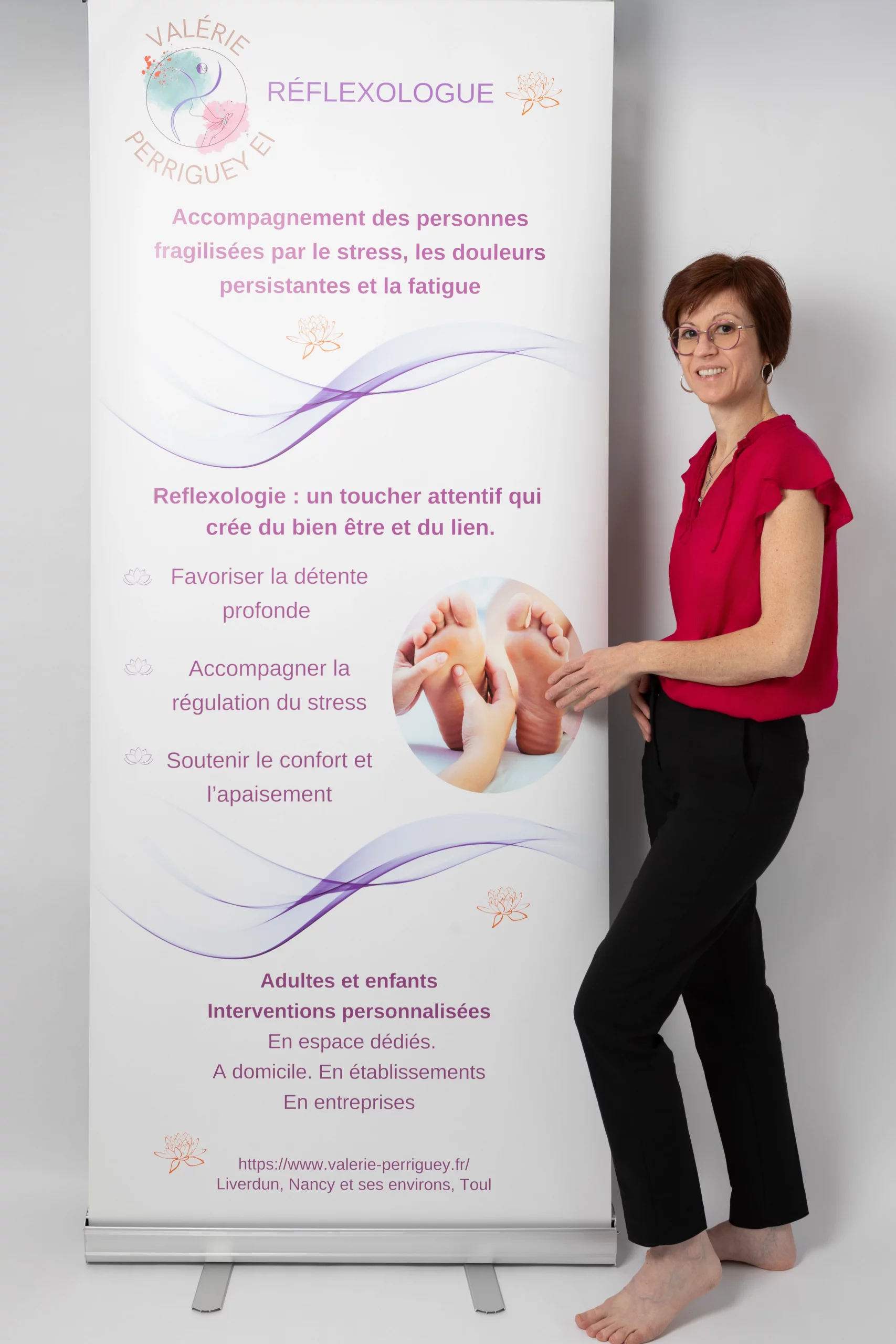 Valérie Perriguey devant une bâche publicitaire, présentant son activité de réflexologue à domicile.